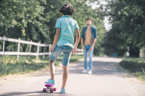 istock Dark-haired boy going to ride a skateboard, his father coming towards him 1256186781