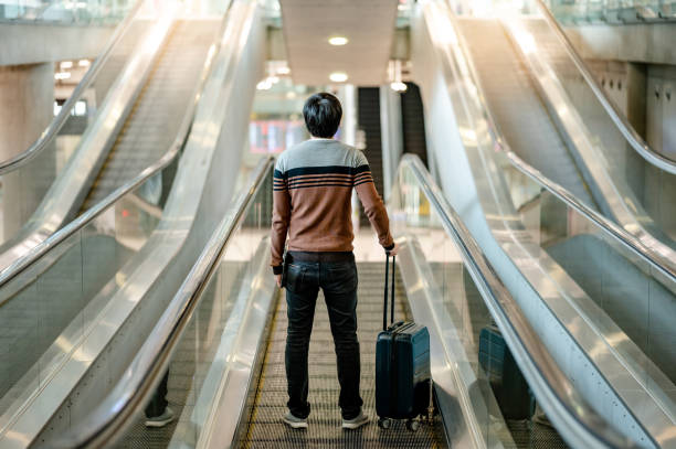 turista maschio che trasporta bagagli in valigia sul viaggiatore - moving walkway escalator airport walking foto e immagini stock