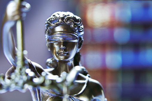 A statue of lady justice in front of a stack of law books that rest out of focus in the background.