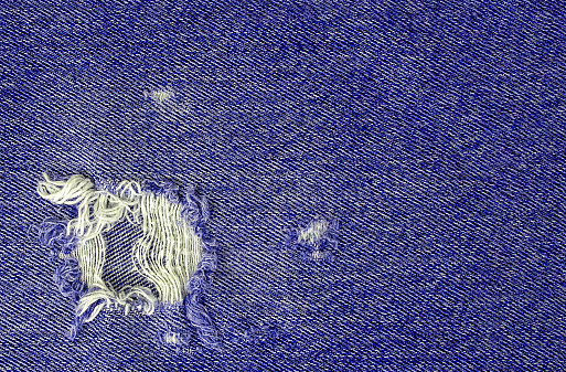 close up of purple denim fabric with frayed hole