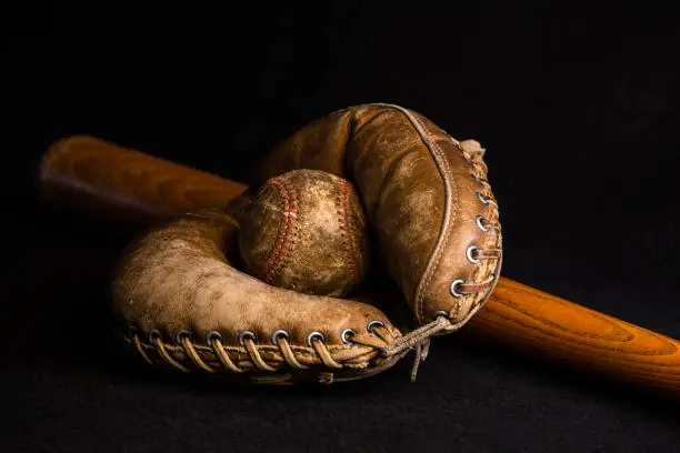 Antique catcher's mitt holding a baseball lying on an old wood bat.