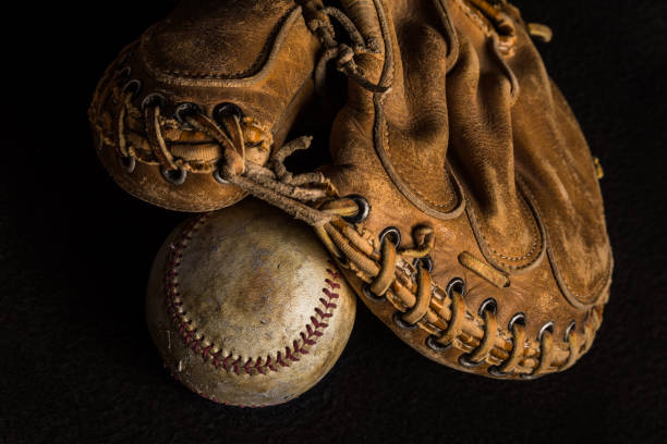 istock Old catchers mitt and worn baseball on black backdrop 1256197677