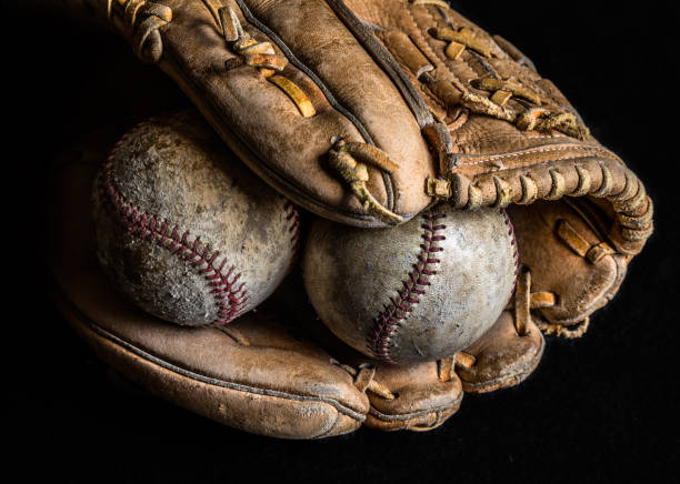 istock Two worn baseballs in an old mitt on black background. 1256197716