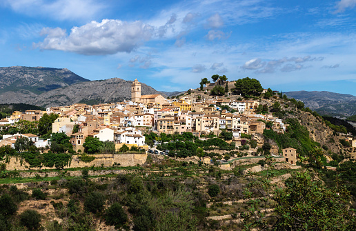 Sunny view of the hills of Polop de Marina with church and castell over green forest at the Costa Blanca, Spain