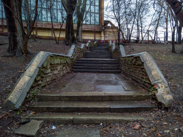 MOSCOW, RUSSIA - MARCH 2, 2020: An old staircase with wet steps leading to an abandoned Soviet building, through bare trees, behind a fence. Palace of Culture of the Hammer and Sickle Factory
