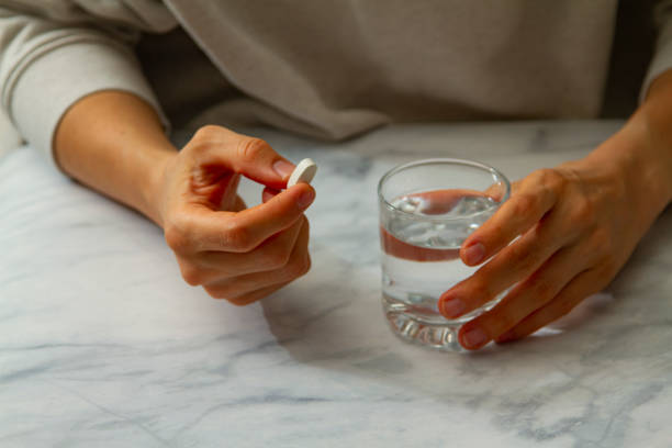 a woman is not sure whether to take this medication A caucasian woman is holding a white pill in one hand and firmly gripping a glass of water on the other hand. She is about to take the pill. Yet either she is in pain or undecided whether to take it. morning after pill stock pictures, royalty-free photos & images