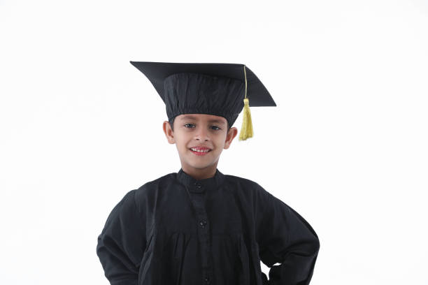 istock Elementary age boy wearing graduation caps and gowns smile while standing with degree in hand 1256223133