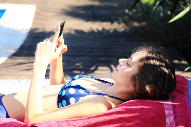 Young woman relaxing by the pool and using smart phone