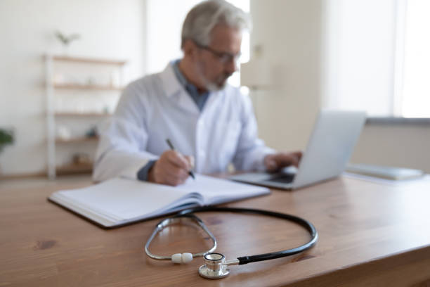 istock Older male doctor work on laptop make notes in journal 1256240161