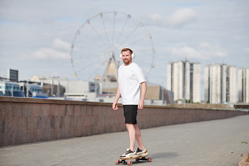 Stylish adult man rides a skateboard on the ramp of the skate park. Practicing skateboarding outdoors in a skate park on a sunny day