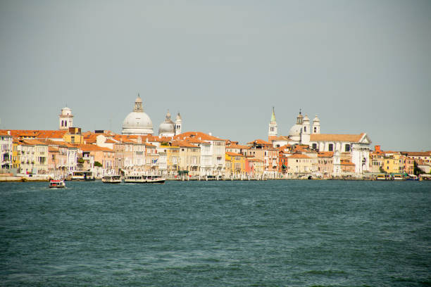 View of the city of Venice Italy, from the vaporetto (public transport boat). Domes and bell towers of diverse churches are to be seen, the distinctive pink and red of the Venice cityscape contrasts with the deep blue of the lagoon's water.