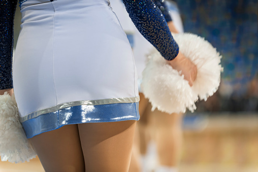 Mid section of cheerleader holding pom pom in basketball court.