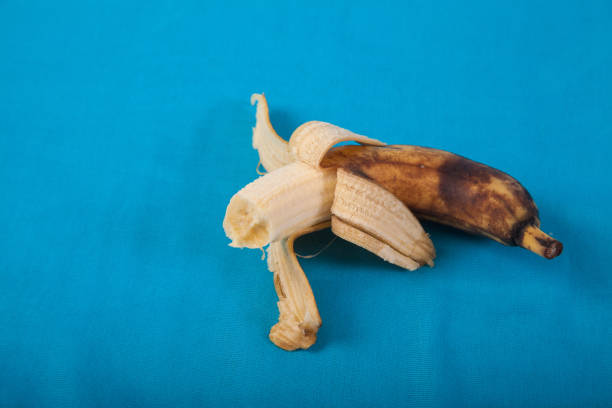 istock Ugly half-peeled bitten banana on a blue background. Copy spaes. 1256247059