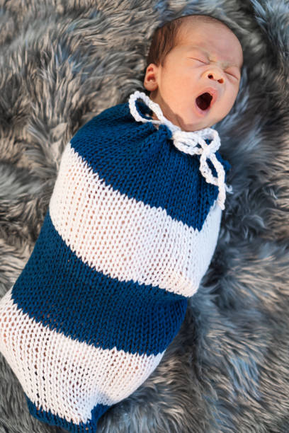 nouveau-né bébé bâillant et swaddled dans une enveloppe en tricot sur le lit - baby yawning asian ethnicity newborn photos et images de collection