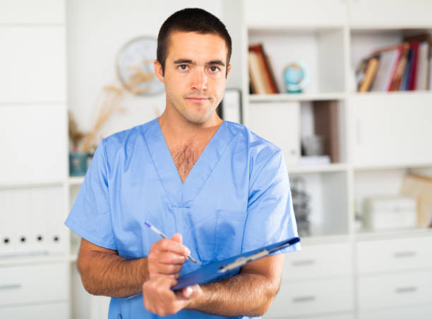 Male nurse filling out medical form on clipboard Portrait of experienced male nurse meeting patients in medical office, filling out medical form on clipboard anamnesis stock pictures, royalty-free photos & images