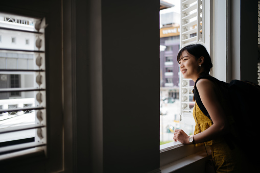 Young asian female tourist with backpack looking out the window and smiling