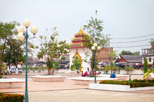 Gate of Pha That Luang and square in Vientiane. Some laotian people are on square. In center  of background is main entrance gate to temple