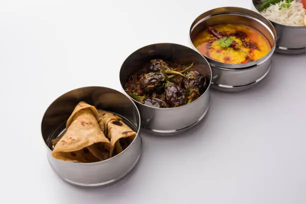 Indian vegetarian Lunch Box or Tiffin made up of stainless steel for office or workplace, includes Dal Fry, Baingan Masala, Rice with chapati and salad