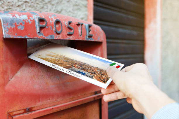 istock Man drop a postcard in a typical red postbox in Venice, Italy. The postcard shows a panorama of Venice. 1256253833