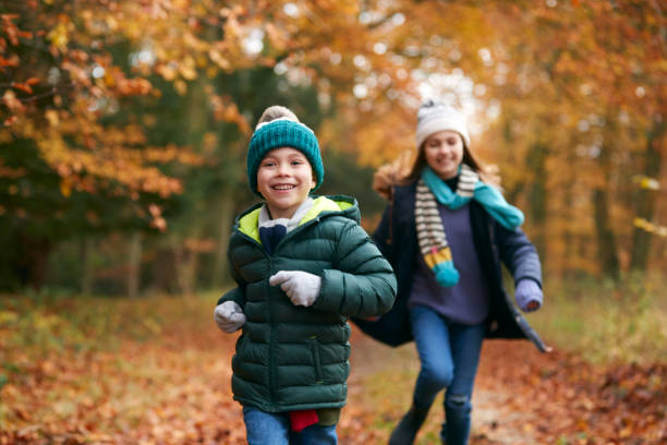 dwoje uśmiechniętych dzieci bawiących się biegając po ścieżce przez jesienne lasy razem - nature forest clothing smiling zdjęcia i obrazy z banku zdjęć