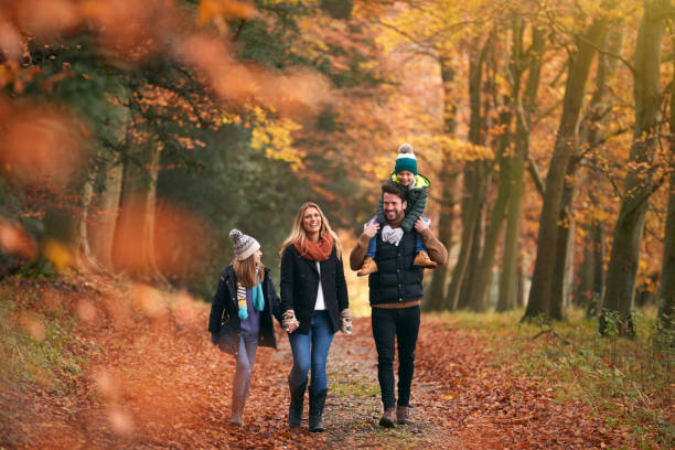 familia caminando a lo largo del camino del bosque de otoño con el padre llevando a su hijo en los hombros - people caucasian sport family fotografías e imágenes de stock