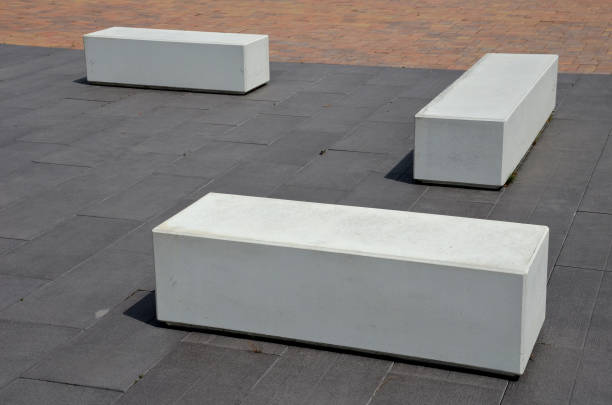 concrete white park bench block shape on dark paving square, clean cast concrete surface gray brown white light barrier against traffic terrorism pedestrian zone - cast in stone imagens e fotografias de stock