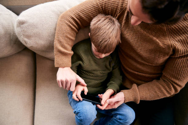 istock Father And Son On Sofa At Home Having Fun Playing Game On Mobile Phone 1256257834