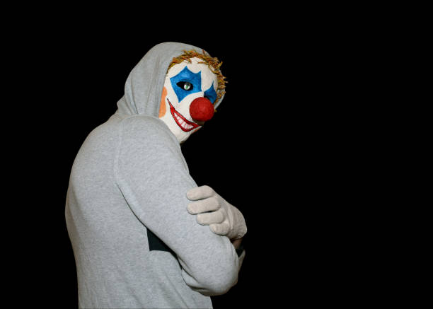 istock Man in a clown mask stands sideways on an isolated black background. 1256259014