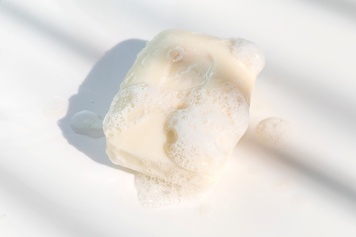 White soap bar and foam on white background in morning light