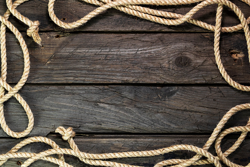 Wooden background from an old board with hemp rope. Ship rope on a dark wooden background. Frame of rope. Top view.