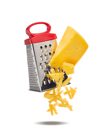 Piece of cheese is rubbed on metal hand grater. Slices of cheese and grater levitate in air. Grater and cheese isolated on white background.