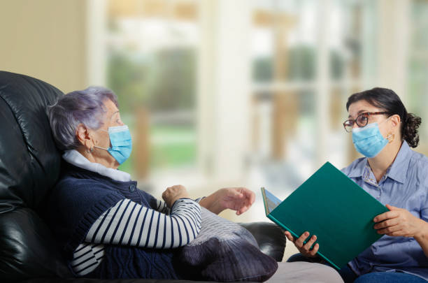A female mature volunteer visits a single senior adult woman during a virus epidemic. stock photo