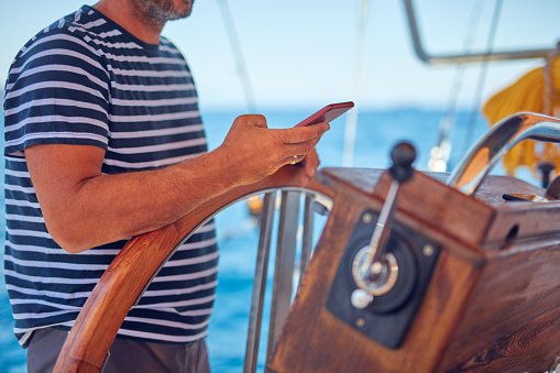 Sailing boat captain using smartphone for navigation on the open sea.