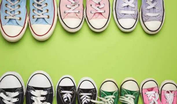 Photo of many multi-colored well-worn textile sneakers of different sizes on a green background