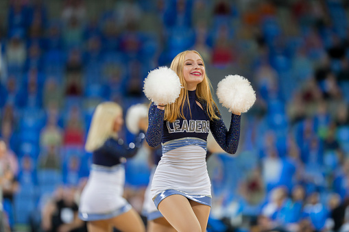 Smiling female cheerleader with pom pom performing in the stadium.