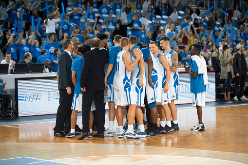 Basketball players in white jersey with their coaches standing on court.