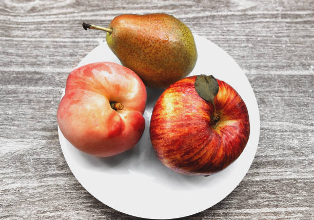 Three green pears and two red apples close up on a dark wooden background
