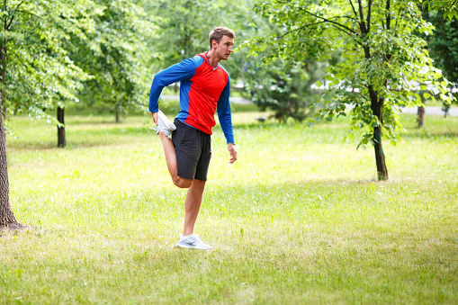 Sport and healthy lifestyle concept - male jogger stretcing muscles in public park.