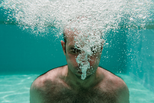 young man diving underwater in a pool making bubbles, summer and fun lifestyle