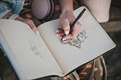 Sketchbook with a drawing of a house close-up. Girl draws with her left hand