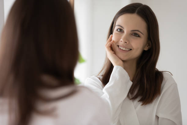 istock Smiling beautiful young woman looking at mirror in bathroom 1256287064