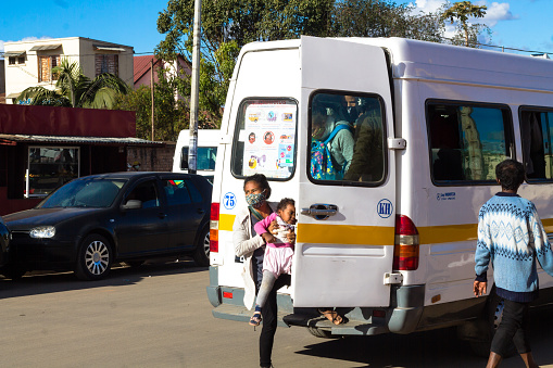 Antananarivo, Madagascar - July 10, 2020: A young woman wearing a mouth mask takes her baby on the bus during the coronavirus epidemic period, East African Islands, Africa.