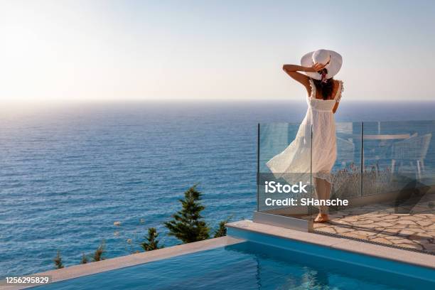 A Elegant Luxury Woman In A White Dress Enjoys The Summer Sunset By The Pool Stock Photo - Download Image Now