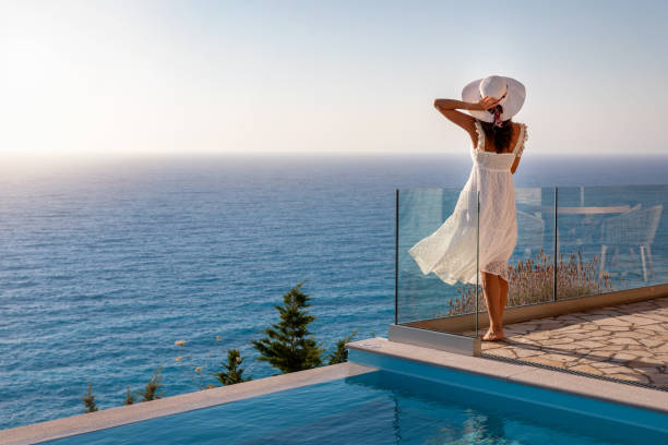 uma mulher elegante e luxuosa em um vestido branco aproveita o pôr do sol de verão à beira da piscina - vacations infinity pool relaxation swimming pool - fotografias e filmes do acervo