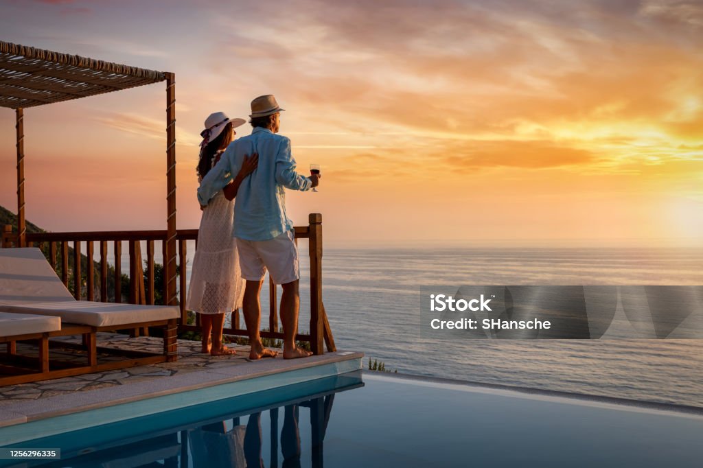 A romantic couple on summer vacation enjos the sunset over the mediterranean sea by the pool A romantic couple on summer vacation enjos the sunset over the mediterranean sea by the pool with a glass of Aperitif Travel Stock Photo