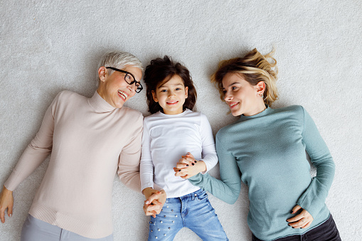 Female members of multi generational family are lying on the carpet and laughing.