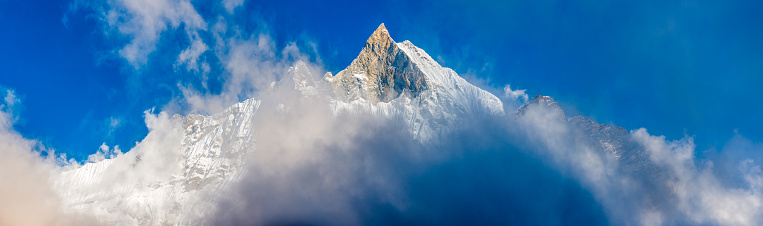 Clouds swirling around the fluted snow ridges, dramatic pinnacles and hanging glaciers of Machapuchare (6993m) deep in the Himalayan mountain wilderness of the Annapurna Conservation Area, Nepal.