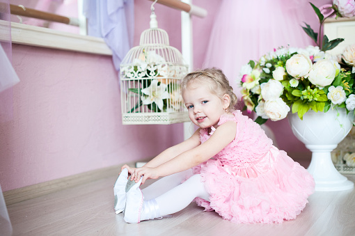 A little ballerina in a dress sits in a dance class on the floor. Near a bouquet of flowers.