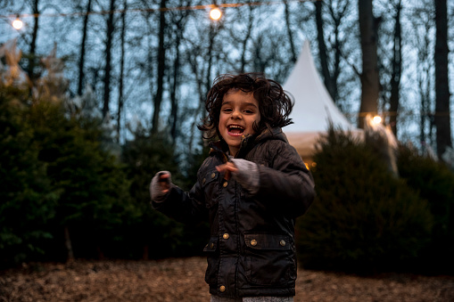 Low lit shot of young boy jumping and playing around at a Christmas tree farm in Newcastle-Upon-Tyne while looking at the camera and smiling.