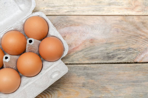 istock Brown chicken eggs in cardboard packaging on wooden background with copy space, view top 1256306314